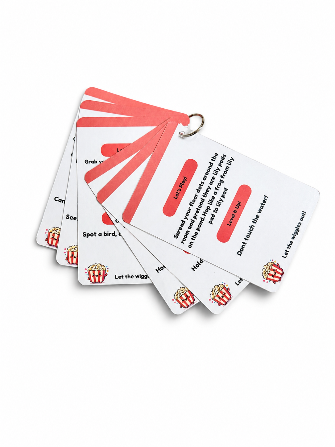 A fanned-out set of white and coral red play prompt cards with a metal ring at the top, photographed on a clean white background.