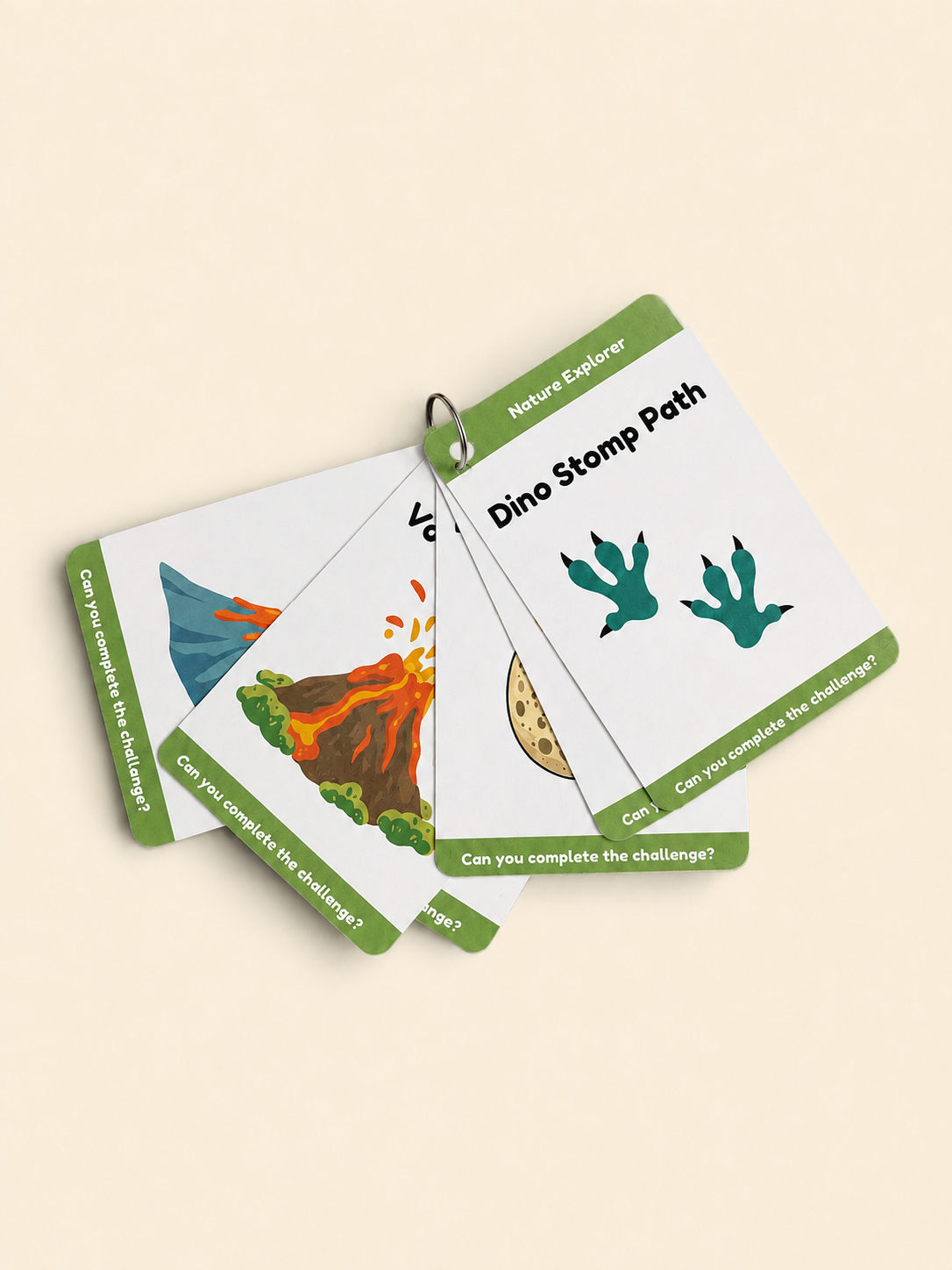 Three educational nature cards fanned out on a light beige background. The cards feature green borders, white centers, and colorful illustrations of a volcano and dinosaur footprints, with the title 'Dino Stomp Path' visible.